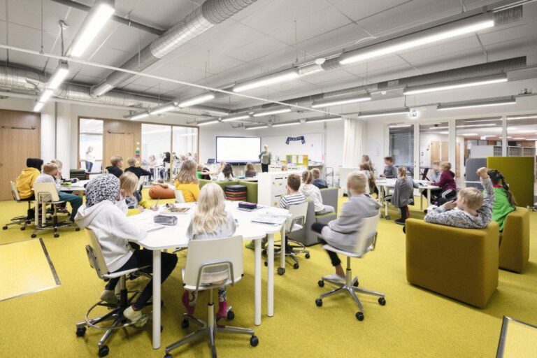 Enseignante accompagnant des élèves réunis en groupes dans une salle de classe finlandaise moderne, illustrant la confiance, l’autonomie et l’apprentissage collaboratif.
